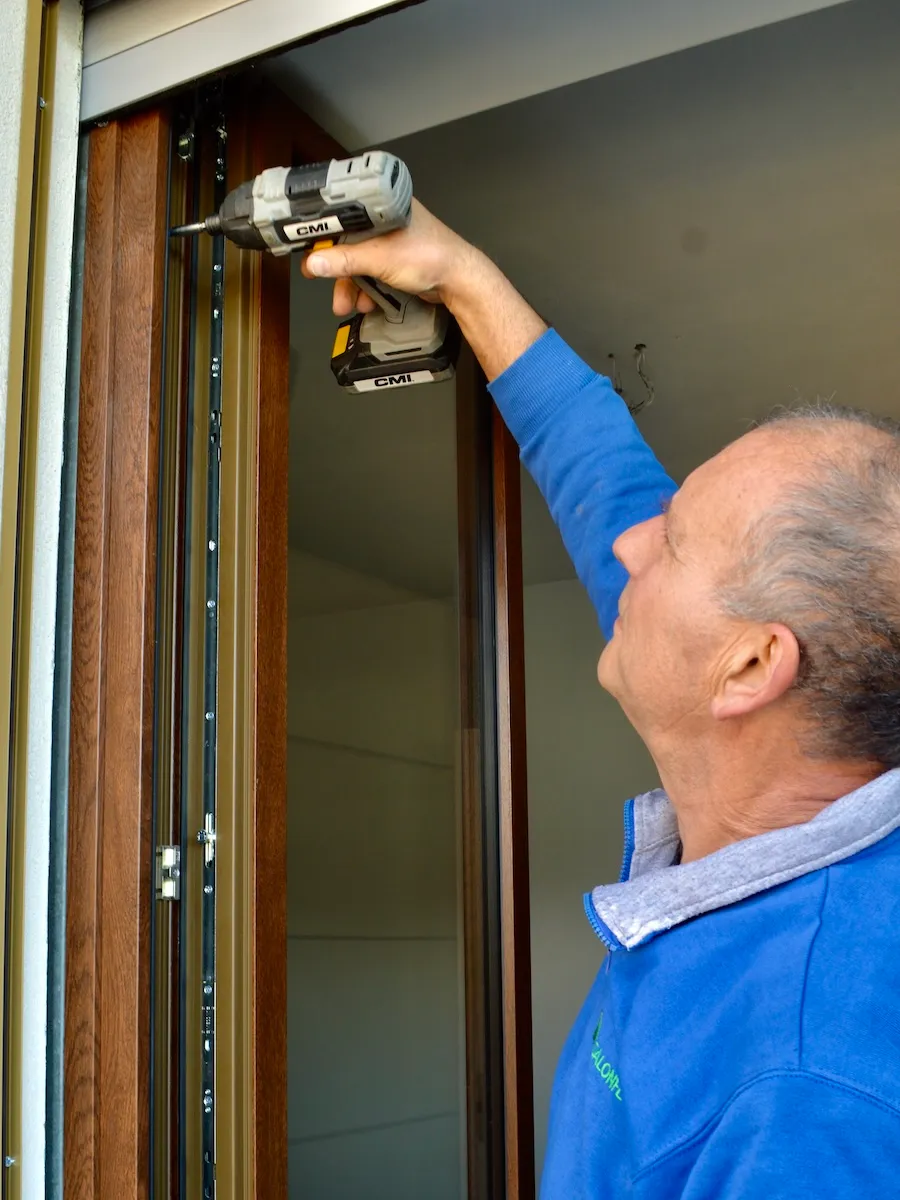 Tecnico Dalonflex avvita il telaio di una zanzariera sulla parte alta di una portafinestra in legno
