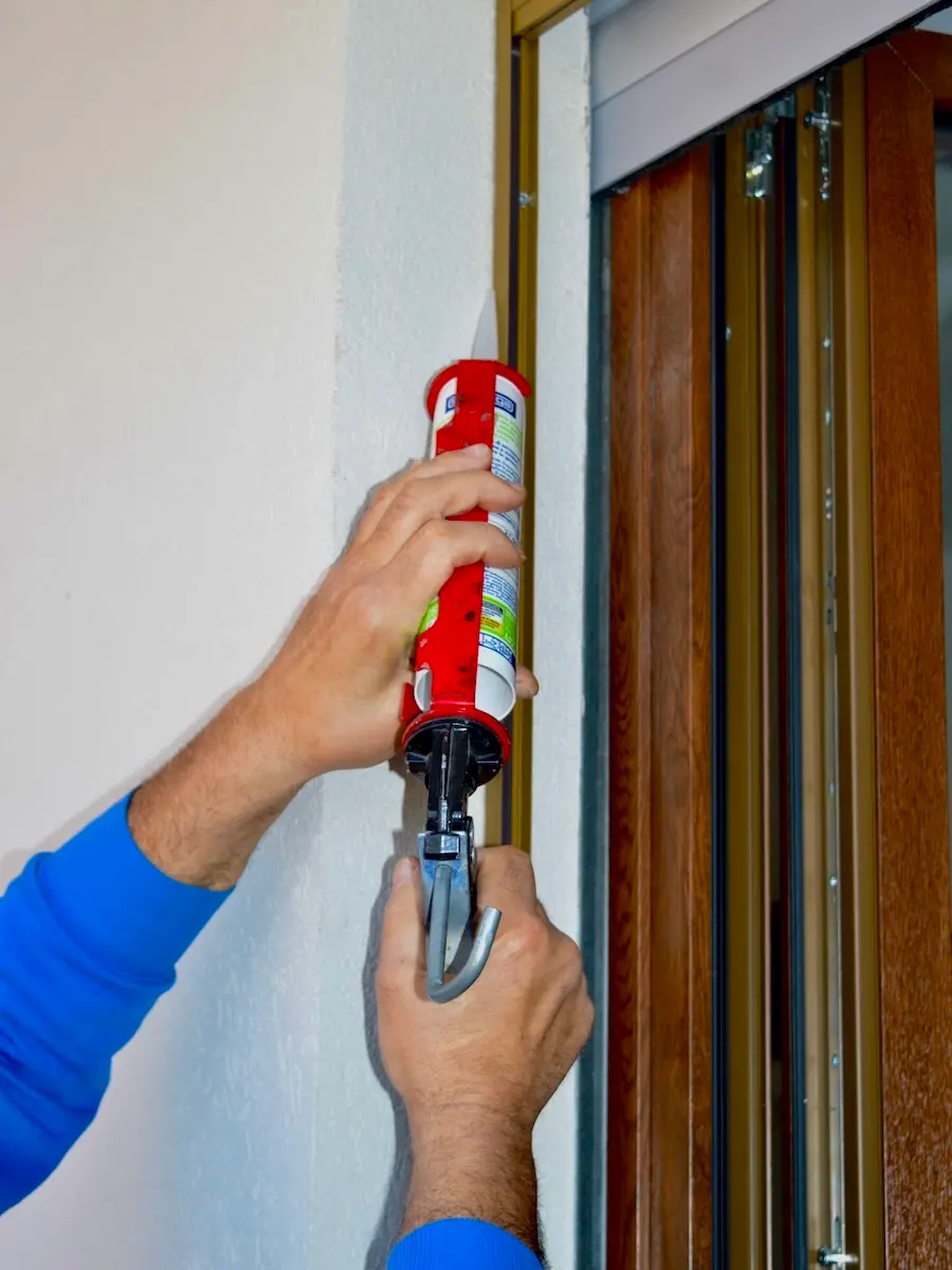 Tecnico Dalonflex applica il silicone lungo il telaio di una zanzariera appena installata su una portafinestra in legno