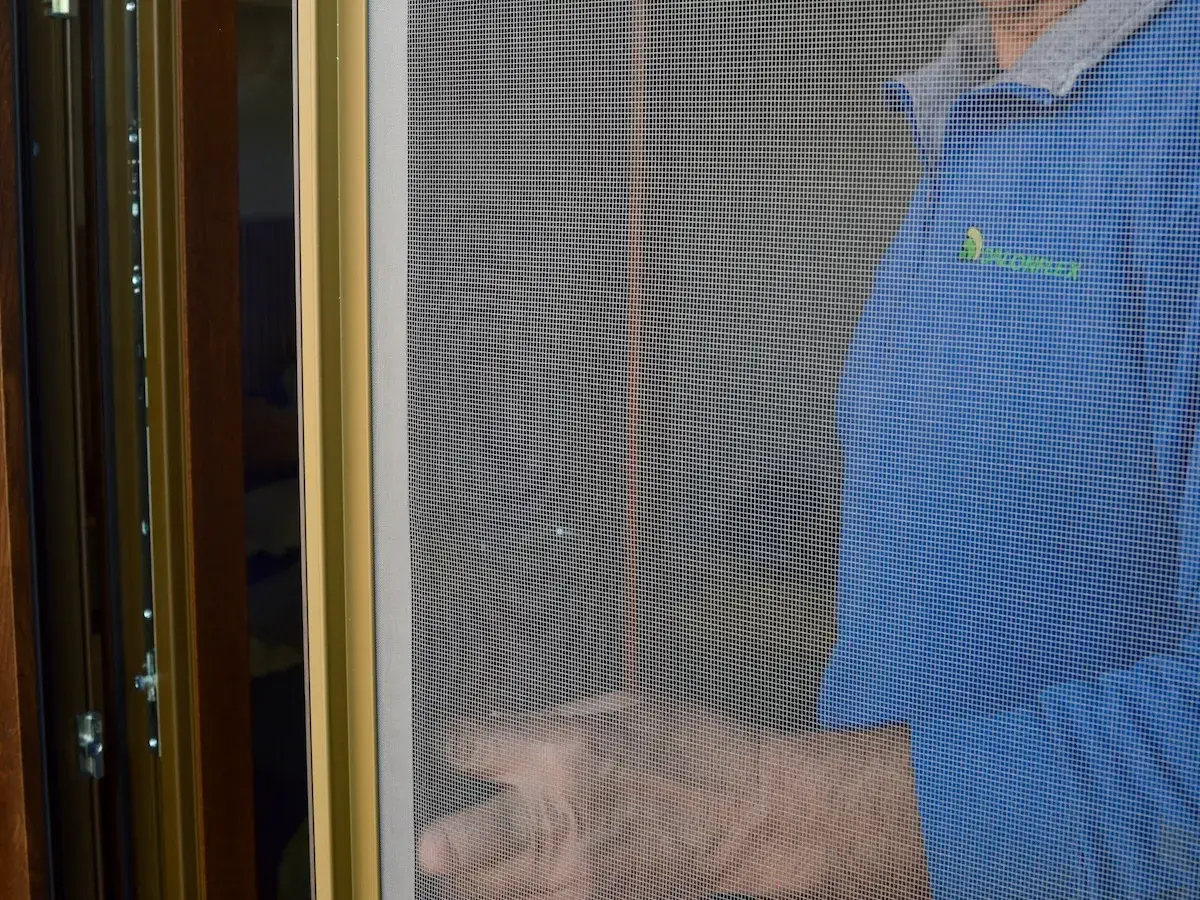 Dettaglio della rete di una zanzariera con il tecnico Dalonflex al lavoro dietro il telaio